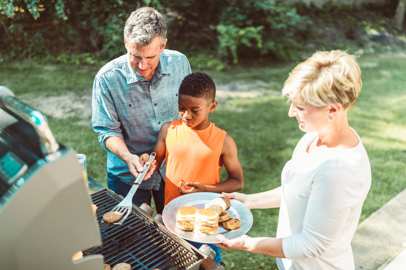 Familie griller burgere i solfylt hage