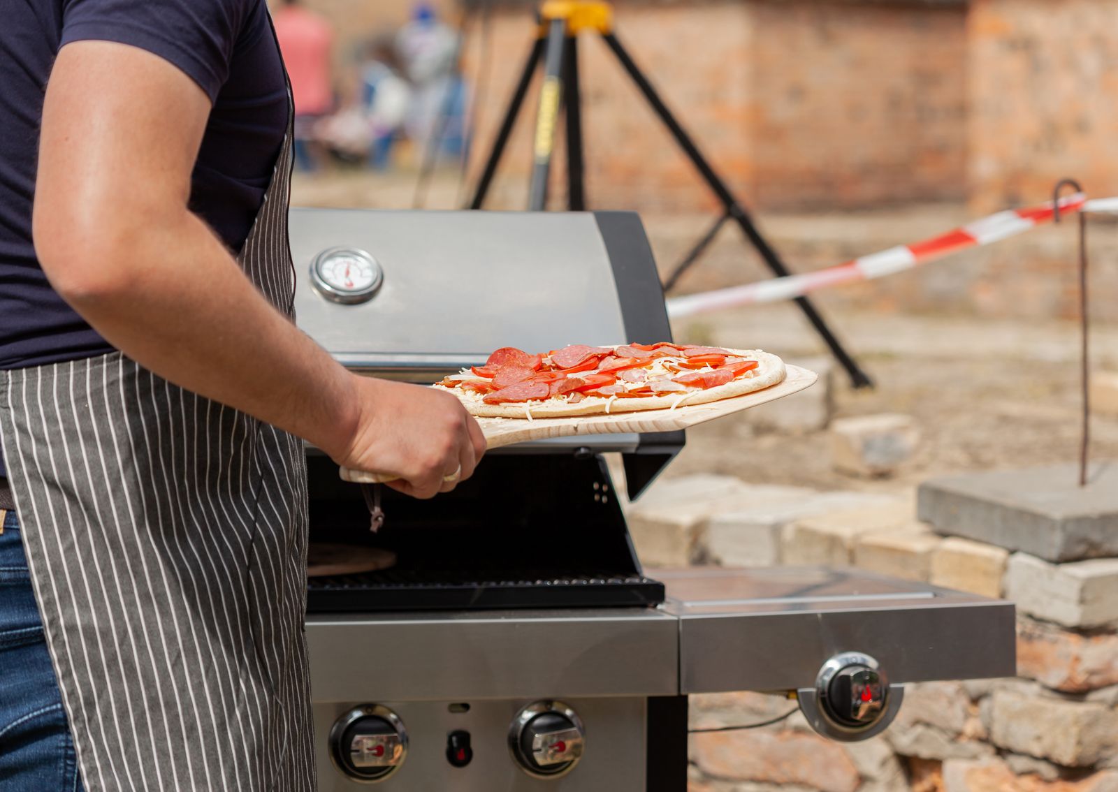 Mann skyter pizza inn i en utendørs pizzaovn med pizzaspade